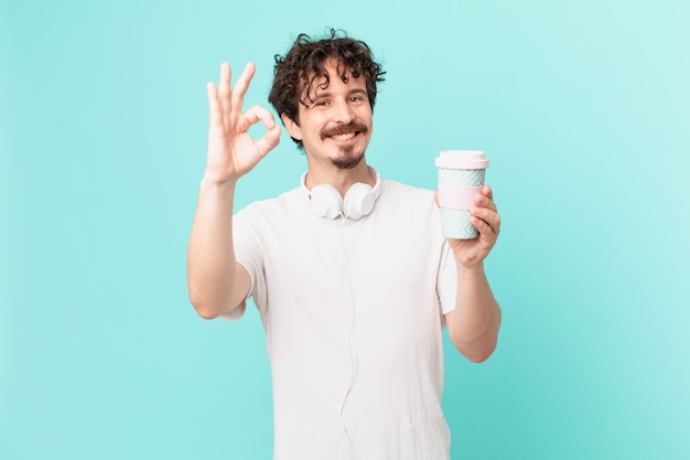 Hombre joven con un café sintiéndose feliz, mostrando aprobación con gesto bien