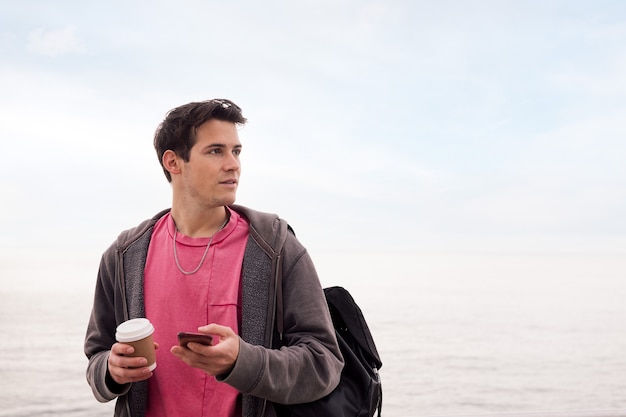 Hombre joven con un café usando un teléfono móvil