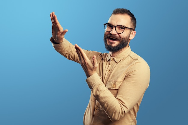 Hombre joven en camisa beige gesticulando tirar dinero divirtiéndose en el estudio