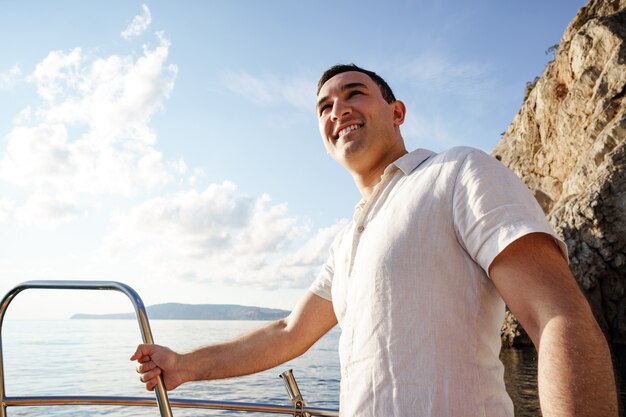 Hombre joven con camisa blanca de pie en el yate de nariz en el mar