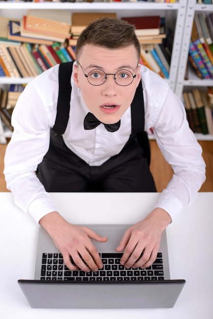 Hombre joven en camisa y pajarita escribiendo algo en la computadora