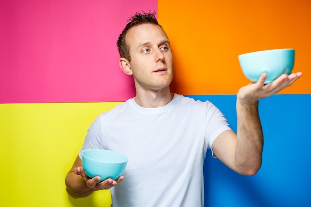 Hombre joven con una camiseta blanca, fondo colorido, utensilios de cocina, cocinero, emociones