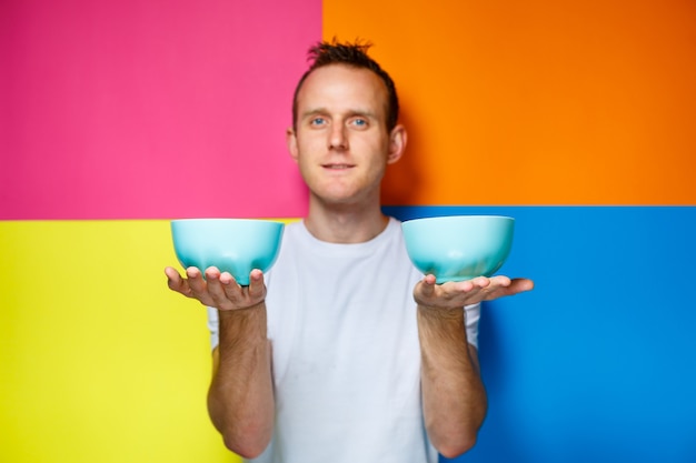 Hombre joven con una camiseta blanca, fondo colorido, utensilios de cocina, cocinero, emociones