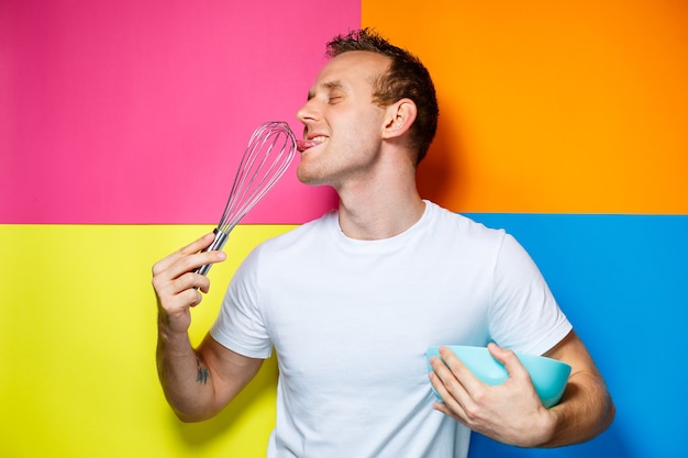 Hombre joven con una camiseta blanca, fondo colorido, utensilios de cocina, cocinero, emociones