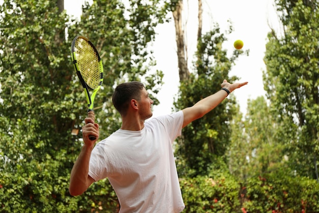 Hombre joven en camiseta blanca sirve la pelota de tenis