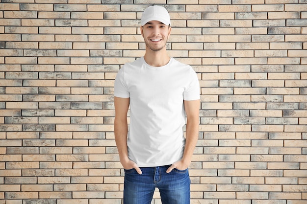 Hombre joven en camiseta elegante contra pared de ladrillo Mockup para diseño