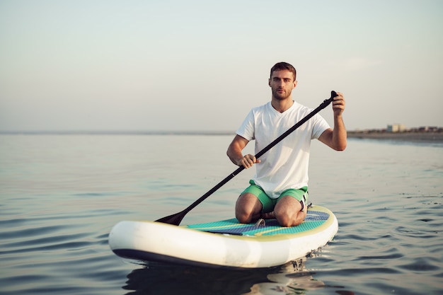 Hombre joven en camiseta y pantalones cortos flotando a bordo de sup