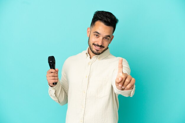 Hombre joven cantante caucásico aislado sobre fondo azul mostrando y levantando un dedo