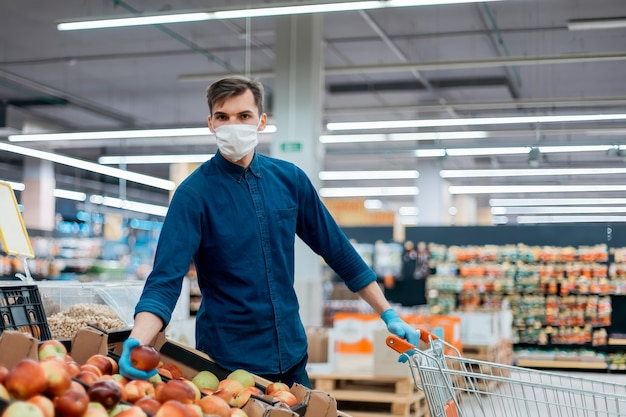 Hombre joven con un carrito de compras recogiendo manzanas