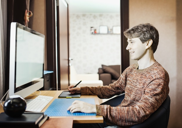 Hombre joven en casa usando una computadora, desarrollador independiente o diseñador que trabaja en casa.