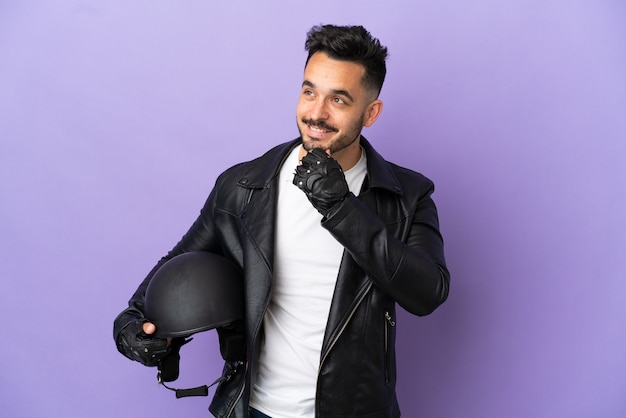 Foto hombre joven con un casco de motocicleta aislado sobre fondo púrpura mirando hacia un lado y sonriendo