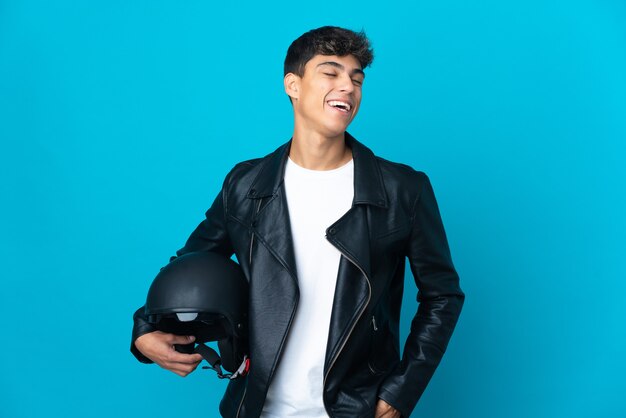 Hombre joven con un casco de motocicleta sobre fondo azul aislado riendo