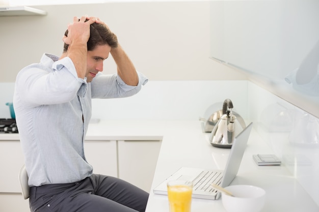 Hombre joven casual concentrado que usa la computadora portátil en cocina