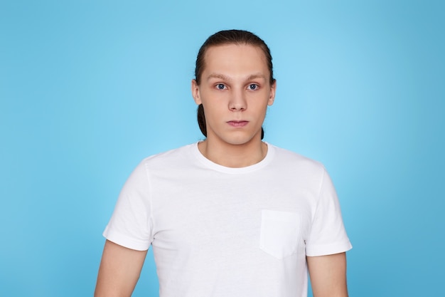 Hombre joven con el ceño fruncido aislado sobre fondo azul. Emociones humanas, expresiones faciales.