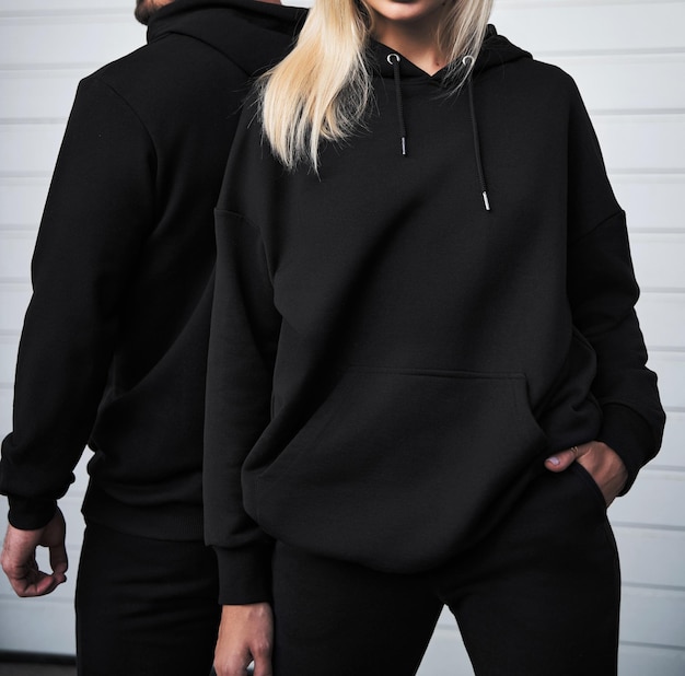 Foto el hombre joven y la chica rubia están parados en una sudadera con capucha oscura para imprimir el logotipo maqueta de ropa para la sudadera con capucha ropa de calle deportiva de otoño