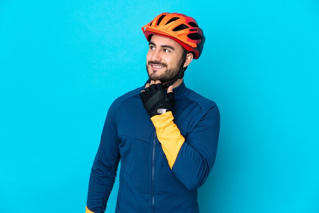 Hombre joven ciclista aislado en la pared azul mirando hacia arriba mientras sonríe