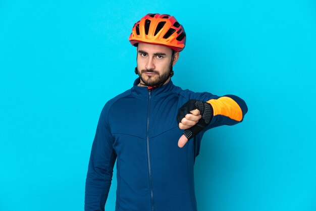 Foto hombre joven ciclista aislado en la pared azul que muestra el pulgar hacia abajo con expresión negativa