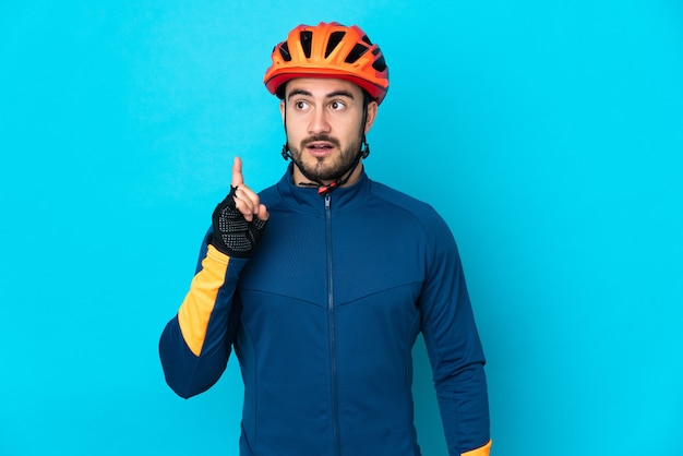 Hombre joven ciclista aislado sobre fondo azul pensando en una idea apuntando con el dedo hacia arriba