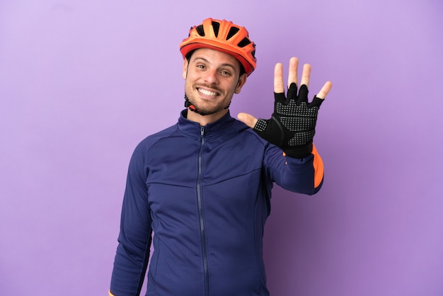 Hombre joven ciclista brasileño aislado sobre fondo púrpura contando cinco con los dedos