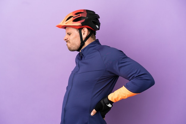 Foto hombre joven ciclista brasileño aislado sobre fondo púrpura que sufre de dolor de espalda por haber hecho un esfuerzo