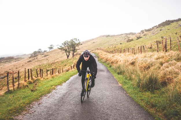 Hombre joven ciclista caucásico corriendo mientras sube una colina en una montaña de niebla.