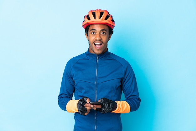 Hombre joven ciclista con trenzas sobre fondo aislado sorprendido y enviando un mensaje