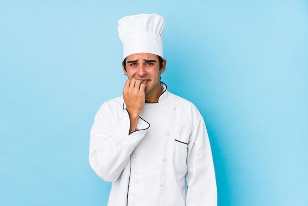 Hombre joven cocinero aislado mordiendo las uñas, nervioso y muy ansioso.