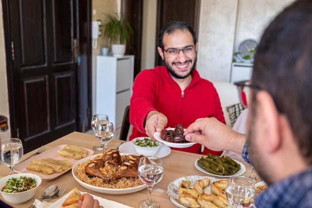 Foto hombre joven comiendo dátiles en la mesa de comedor con su familia durante el iftar dando dátiles