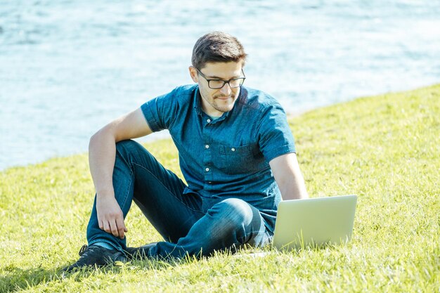 Hombre joven con computadora portátil al aire libre sentado en el césped Concepto de trabajo remoto
