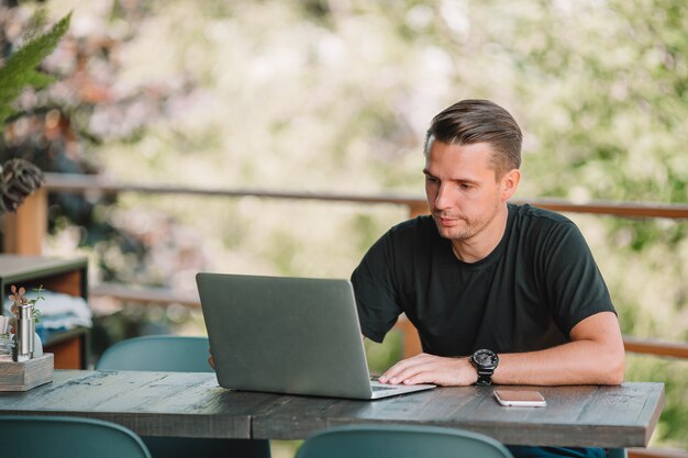 Hombre joven con la computadora portátil en café al aire libre que bebe el café.