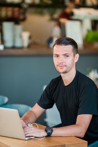 Hombre joven con la computadora portátil en café de consumición del café al aire libre. Hombre que usa teléfono inteligente móvil.