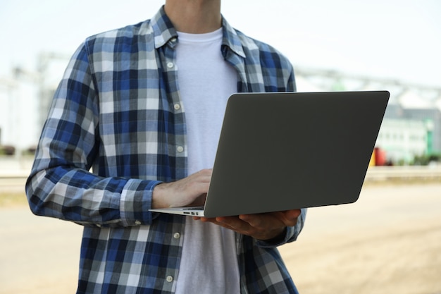 Hombre joven con la computadora portátil contra silos de grano. Negocio de la agricultura