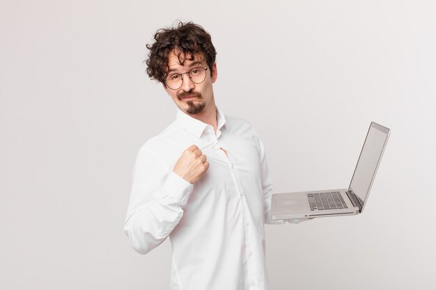 Hombre joven con una computadora portátil que parece arrogante, exitoso, positivo y orgulloso