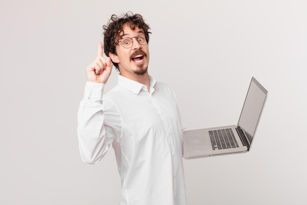 Hombre joven con una computadora portátil que se siente como un genio feliz y emocionado después de darse cuenta de una idea