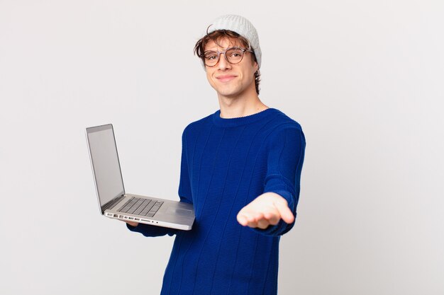 Hombre joven con una computadora portátil sonriendo felizmente con amigable y ofreciendo y mostrando un concepto