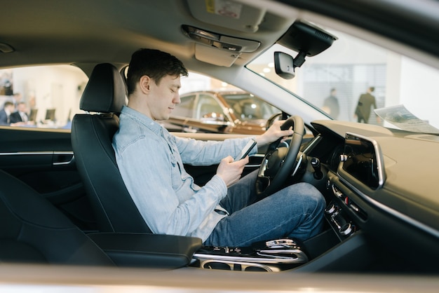 Hombre joven confidente que usa el teléfono móvil se sienta detrás del volante del coche