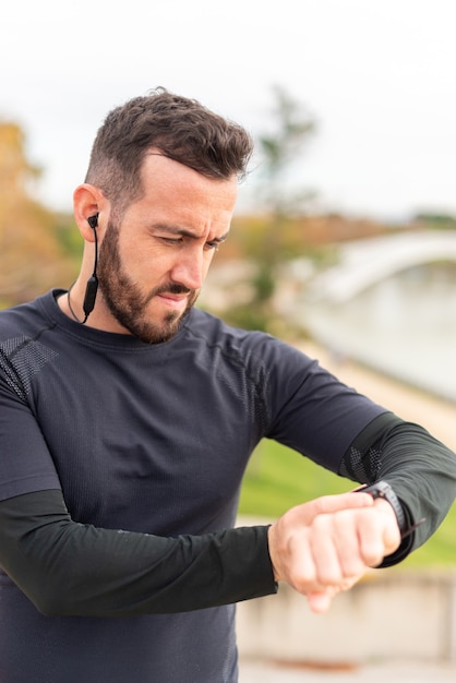 Hombre joven corredor con auriculares entrenando y comprobando el cronómetro.