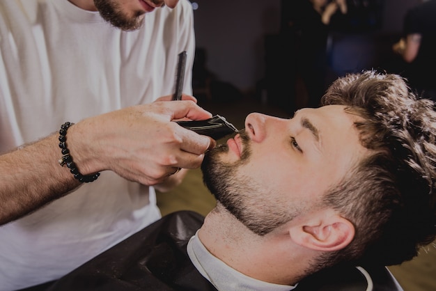 Hombre joven con corte de pelo de moda en peluquería. Barber hace el corte de pelo y la barba.