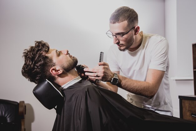 Hombre joven con corte de pelo de moda en peluquería. Barber hace el corte de pelo y la barba.