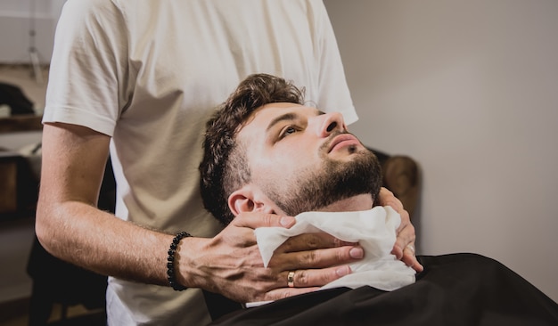 Hombre joven con corte de pelo de moda en peluquería. Barber hace el peinado y la barba.