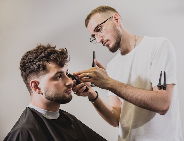 Hombre joven con corte de pelo de moda en peluquería. Barber hace el peinado y la barba.