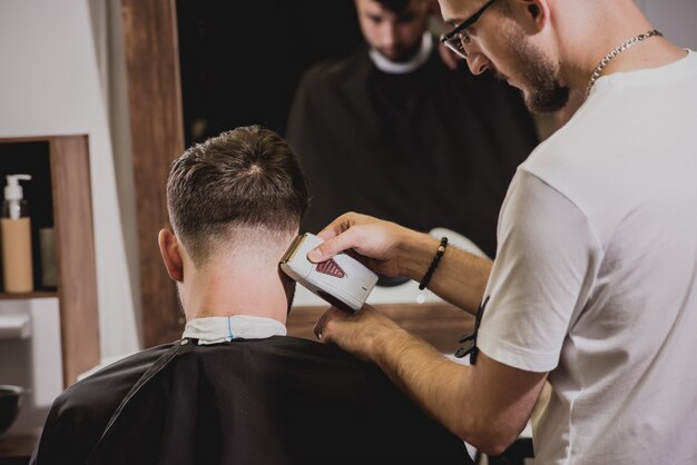 Hombre joven con corte de pelo de moda en peluquería. Barber hace el peinado y la barba.