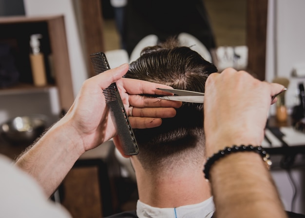 Hombre joven con corte de pelo de moda en peluquería. barber hace el peinado y la barba.