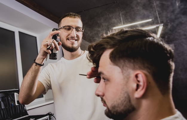 Hombre joven con corte de pelo de moda en peluquería. Barber hace el peinado y la barba.