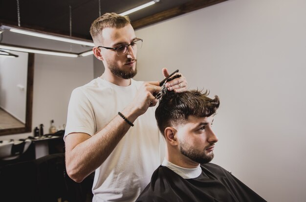 Hombre joven con corte de pelo de moda en peluquería. Barber hace el peinado y la barba.