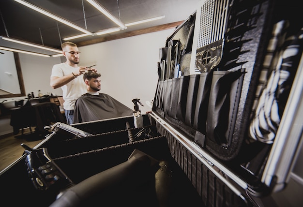 Hombre joven con corte de pelo de moda en peluquería. Barber hace el peinado y la barba.