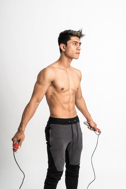 Foto hombre joven con cuerpo musculoso sosteniendo saltar la cuerda con dos manos pararse mirando hacia adelante y mirar hacia un lado