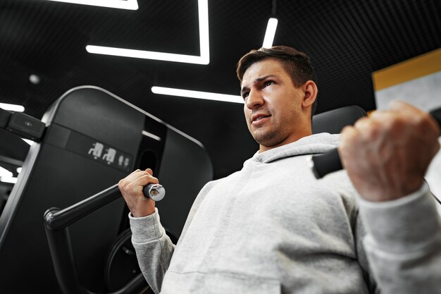 Hombre joven culturista en forma haciendo entrenamiento de brazos en el gimnasio en la máquina