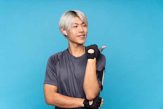 Hombre joven deporte asiático sobre azul aislado apuntando hacia el lado para presentar un producto