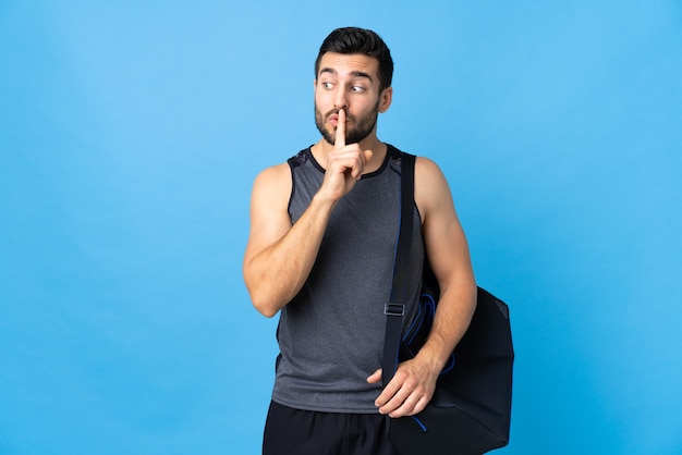 Hombre joven deporte con bolsa de deporte aislado sobre fondo azul que muestra un gesto de silencio poniendo el dedo en la boca